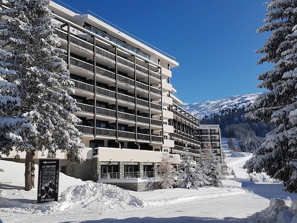 Un hotel de varios pisos con balcones, rodeado de árboles y montañas cubiertas de nieve.