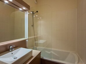 Un baño con un lavamanos blanco, un espejo y una zona de ducha con paredes de vidrio.