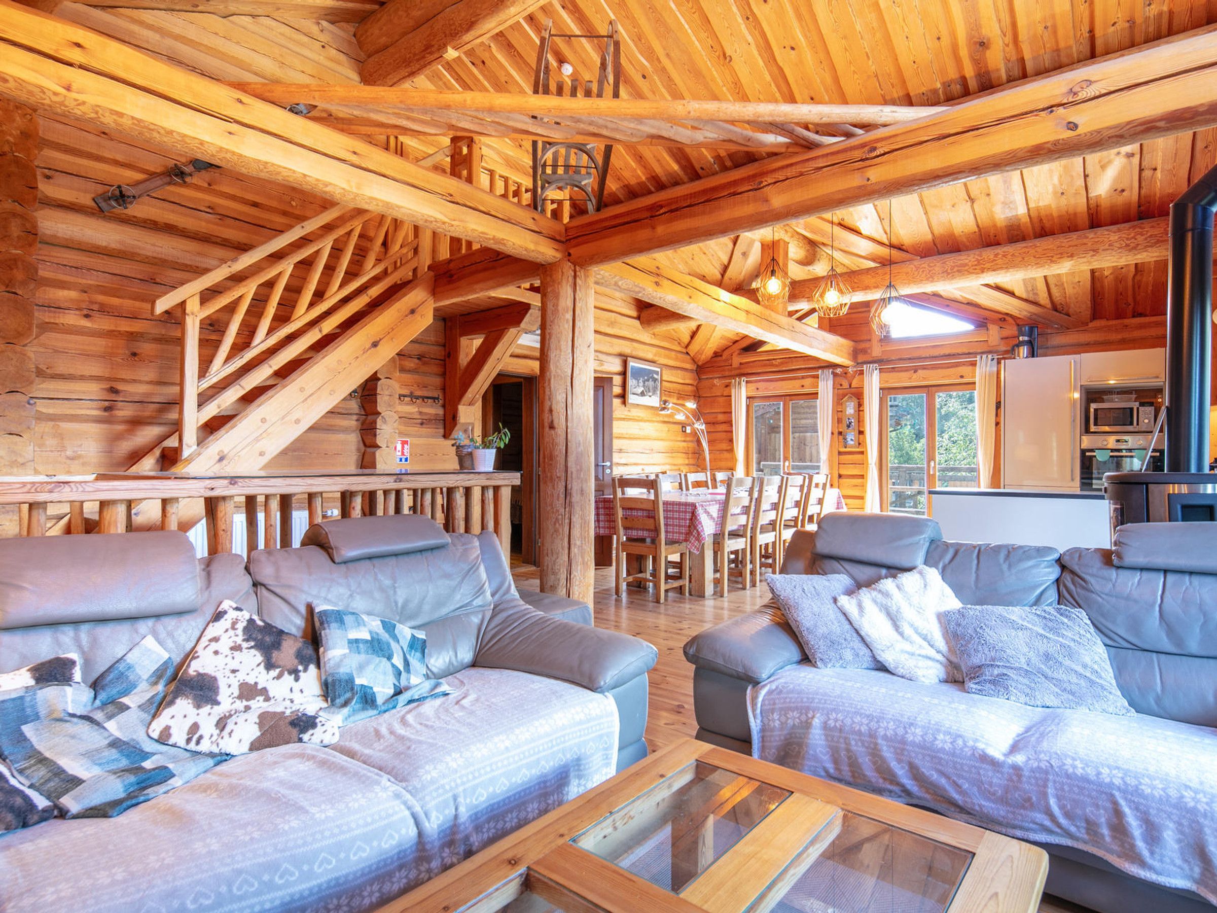 A log cabin interior with a dining area, kitchen, and seating with a glass coffee table.