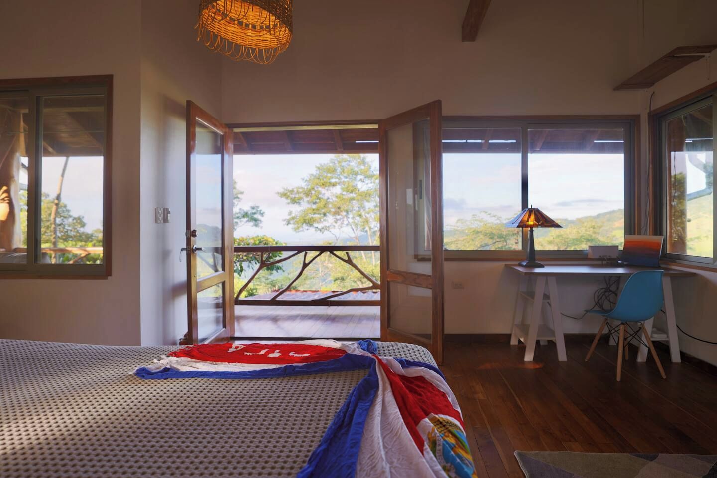 A bedroom with a bed, a desk, and a view of the outdoors.