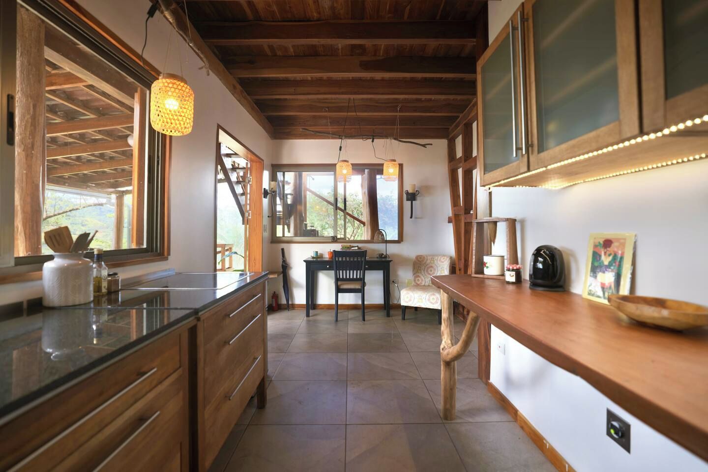 A kitchen with wooden cabinets, a countertop, a dining area with a table and chairs, and a window with a view.