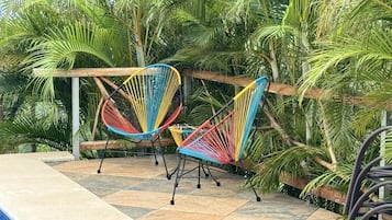 Zona junto a la piscina con dos hamacas de colores y una pérgola de madera.