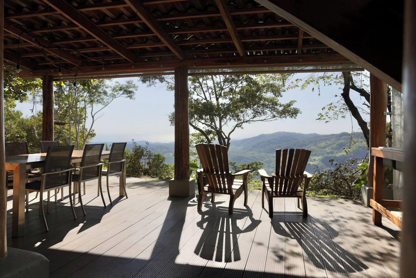 Un área de estar al aire libre con terraza de madera, sillas y una mesa, con vistas a un paisaje montañoso.