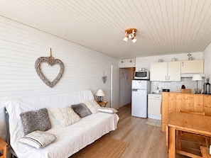 A compact living space with a sofa, a dining table, a kitchen area with a microwave, and a ceiling fan. - Apartment, panoramic view - 4/5 guests (Chamrousse)