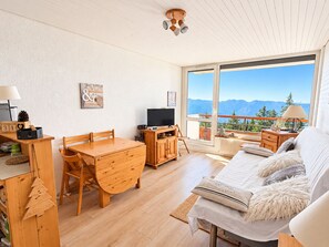A modern living room with a wooden dining table, a sofa, and a television. - Apartment, panoramic view - 4/5 guests (Chamrousse)