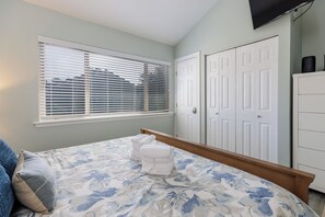 Quarto com cama, janela com persianas, guarda-roupa e televisão na parede.