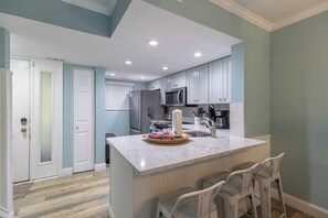 A modern kitchen with a marble countertop, stainless steel appliances, and a central island with bar stools. - 705 Tanglewood: 2BD/2.5BA/Hosts 6 (Hilton Head Island)