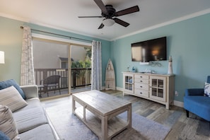 Sala de estar com sofá, mesa de centro, televisão e varanda com porta de correr.