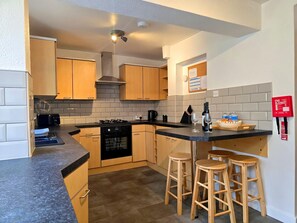 A modern kitchen with wooden cabinets, a black stove, and a small island with stools. - Centrally Located Town House - Pass the Keys (Bangor)