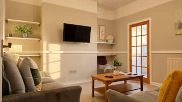 A living room with a sofa, a coffee table, a TV mounted on the wall, and a door with a window.