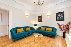 Ein Wohnzimmer mit zwei sofas in Türkis, einem Glastisch und einer Kronleuchter.