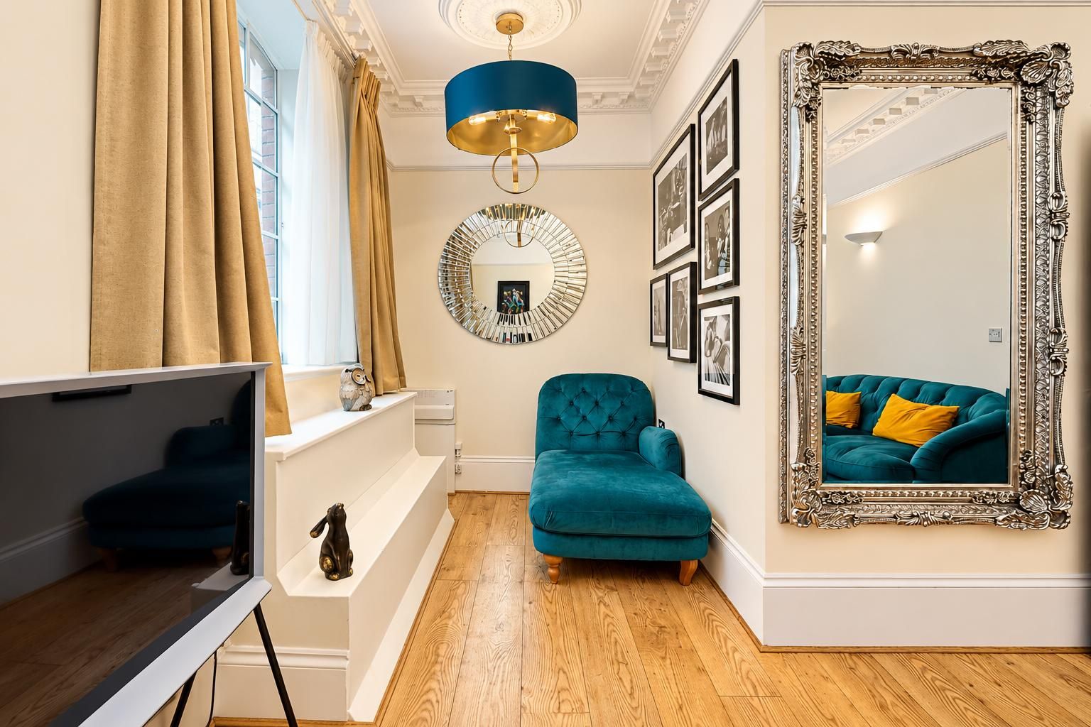 A room with a teal sofa, a large ornate mirror, and a modern chandelier.