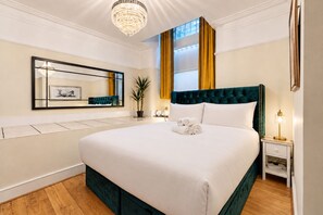 Habitación de hotel con una cama grande, una mesita de noche, una lámpara, un espejo y una planta en maceta.