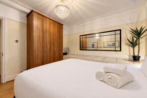 Ein Schlafzimmer mit einem großen Bett, einem Holzschrank, einer Chandelüstere, einem Topfpflanzen und einem gerahmten Kunstwerk an der Wand.