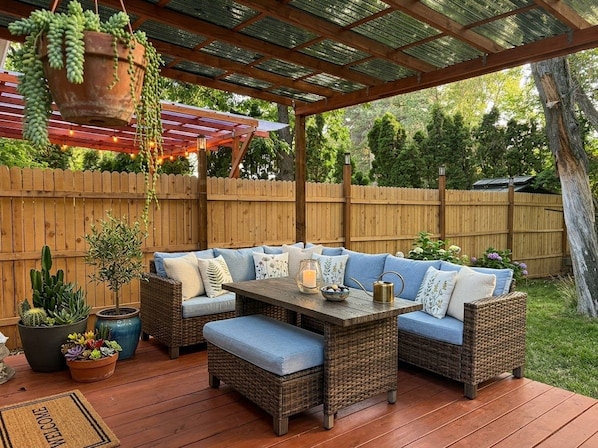 An outdoor patio with a wooden deck, wicker furniture, and potted plants.