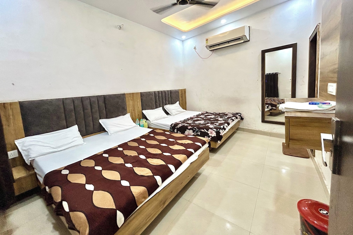 A hotel room with two beds, a ceiling fan, an air conditioning unit, a bedside table, and a mirror.