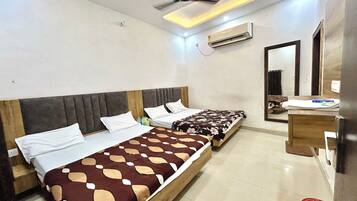A hotel room with two single beds, a ceiling fan, an air conditioning unit, a bedside table, and a mirror.