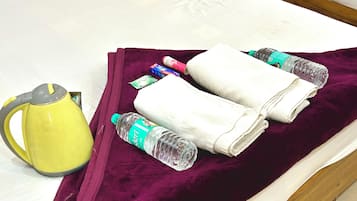 Uma cama com um cobertor roxo, uma chaleira amarela, uma garrafa de água e um pacote de lenços.