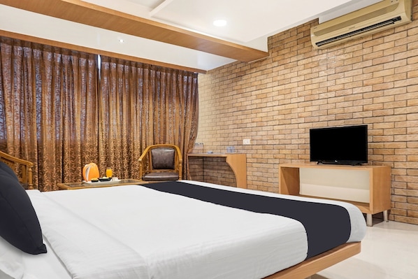 A hotel room with a large bed, a television on a wooden stand, a brick wall, and a window with curtains. - Townhouse OAK Gharonda Residency (Pune)