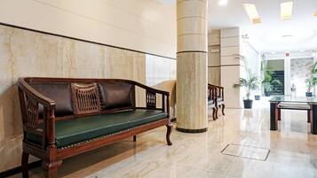 A lobby with a wooden bench, marble walls, and a glass table.