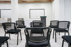 A conference room with a whiteboard, a podium, and several black mesh chairs arranged in rows. - Townhouse OAK Gharonda Residency (Pune)