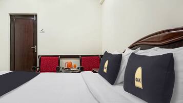 Habitación de hotel con una cama, una puerta de madera, una silla roja y una pequeña mesa con una tetera y un vaso de jugo de naranja.