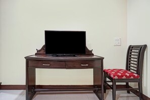 Un escritorio de madera con un televisor, una silla con un cojín estampado y un enchufe de pared.