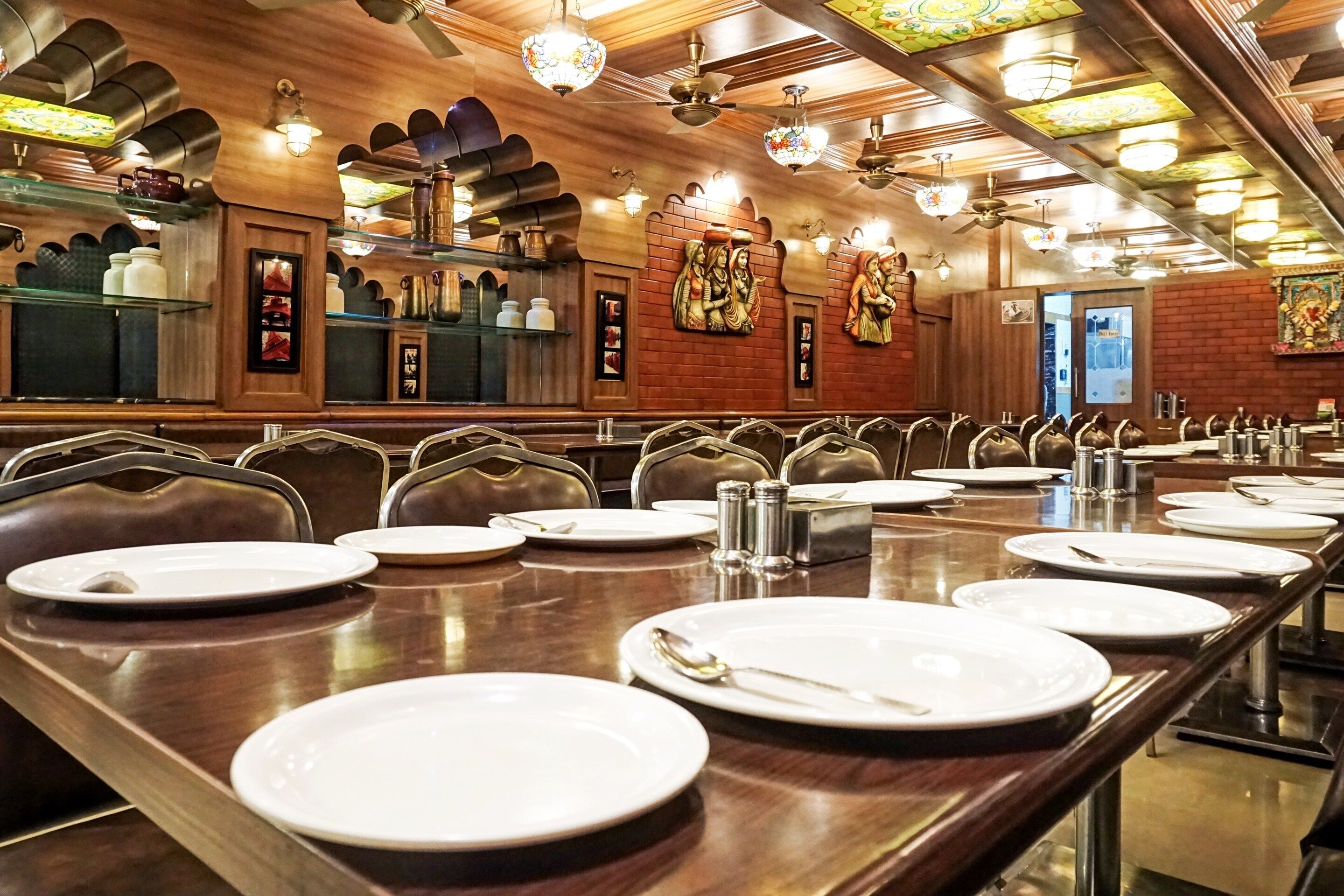 A restaurant with long wooden tables, metal chairs, and a brick wall with decorative wall art.