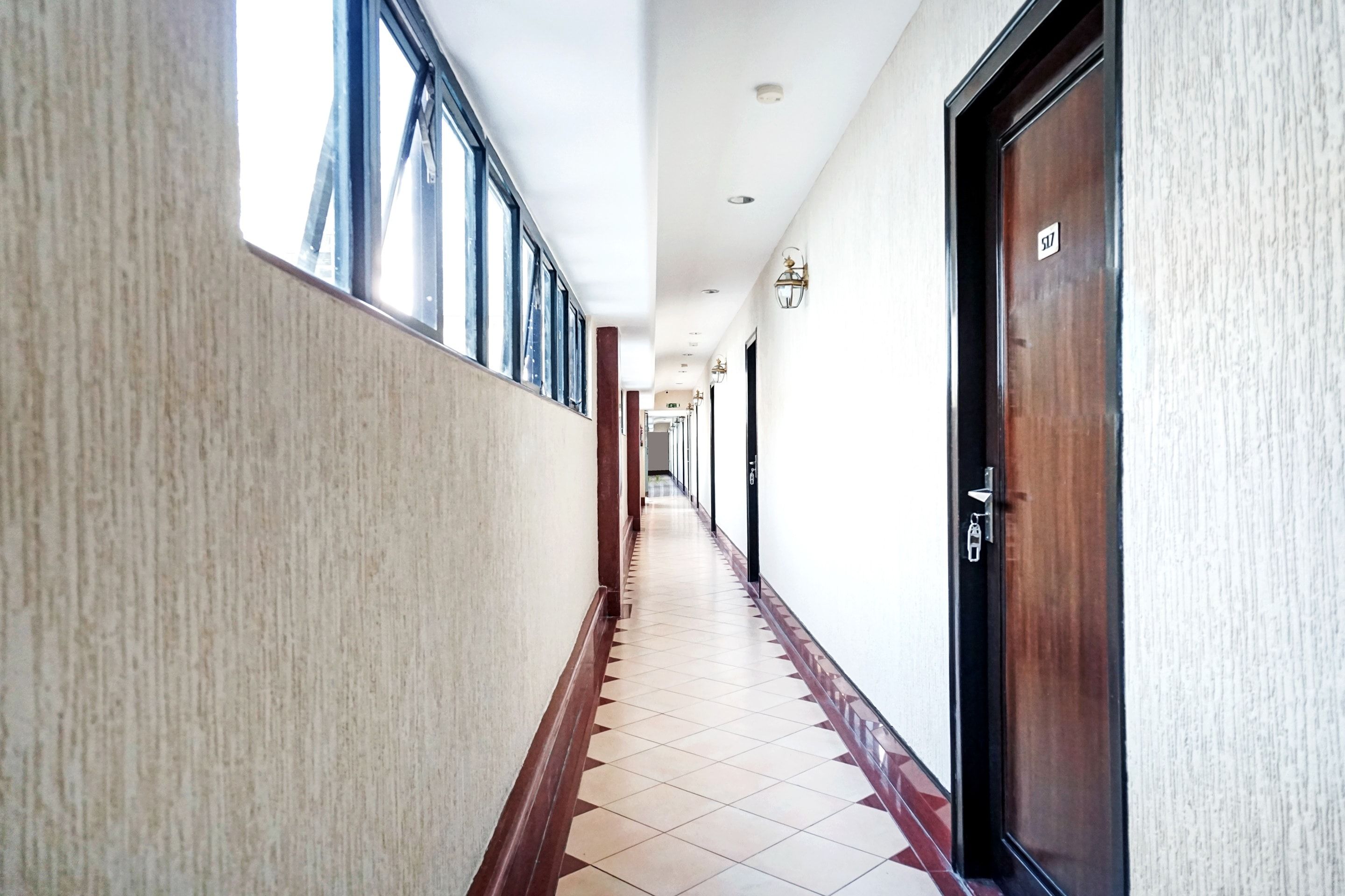 A hotel corridor with a tiled floor, a wooden door on the right, and a window on the left.