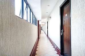 A hotel corridor with a tiled floor, a wooden door on the right, and a window on the left.