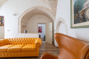 A modern interior with a yellow sofa, a brown chair, and a kitchen area with a white door. - Roof-Top Maisonette | Old Town by TrulloVista (Martina Franca)