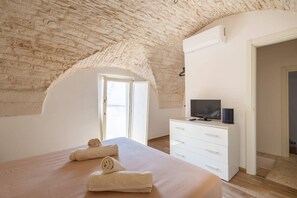 A bedroom with a sloped ceiling, a bed with towels, a TV on a dresser, and a door leading to another room. - Roof-Top Maisonette | Old Town by TrulloVista (Martina Franca)
