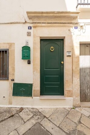 Une porte verte avec un heurtoir en laiton, une boîte aux lettres et une plaque indiquant le numéro de la maison.