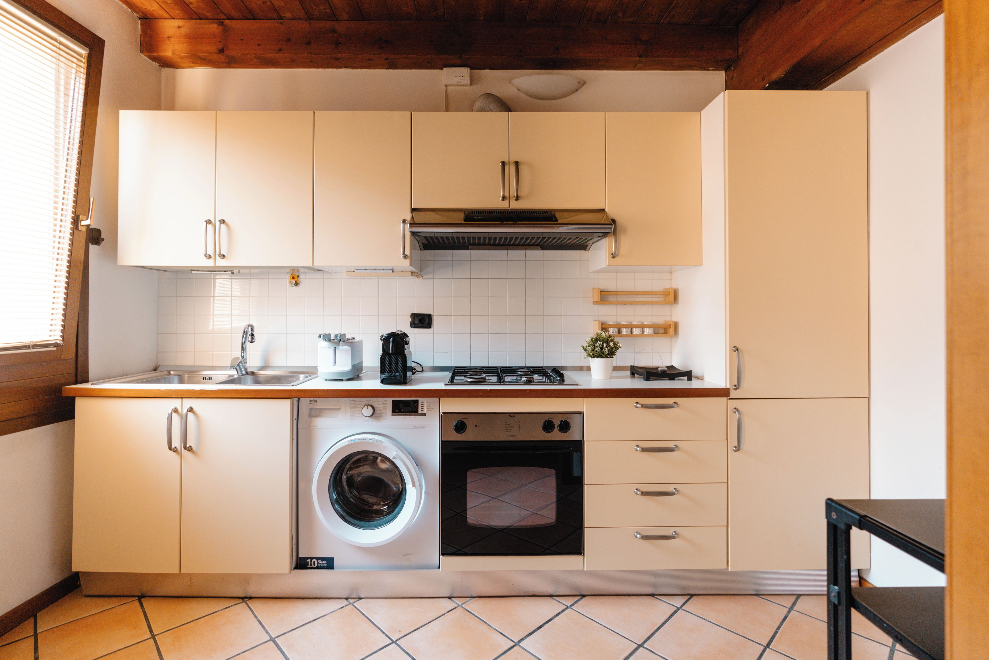 Una cucina compatta con mobili bianchi, una lavatrice integrata, un fornello e un lavandino.