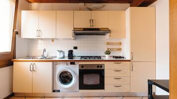 Una cucina compatta con mobili bianchi, una lavatrice integrata, un fornello e un lavandino.