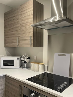 Une cuisine moderne dotée d’un four à micro-ondes encastré, d’une plaque de cuisson en verre, de meubles en bois et d’une hotte aspirante en acier inoxydable.