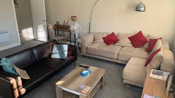 Una sala de estar con un sofá de cuero negro, un sofá color beige con cojines rojos, una mesa de centro de madera y una lámpara de pie.
