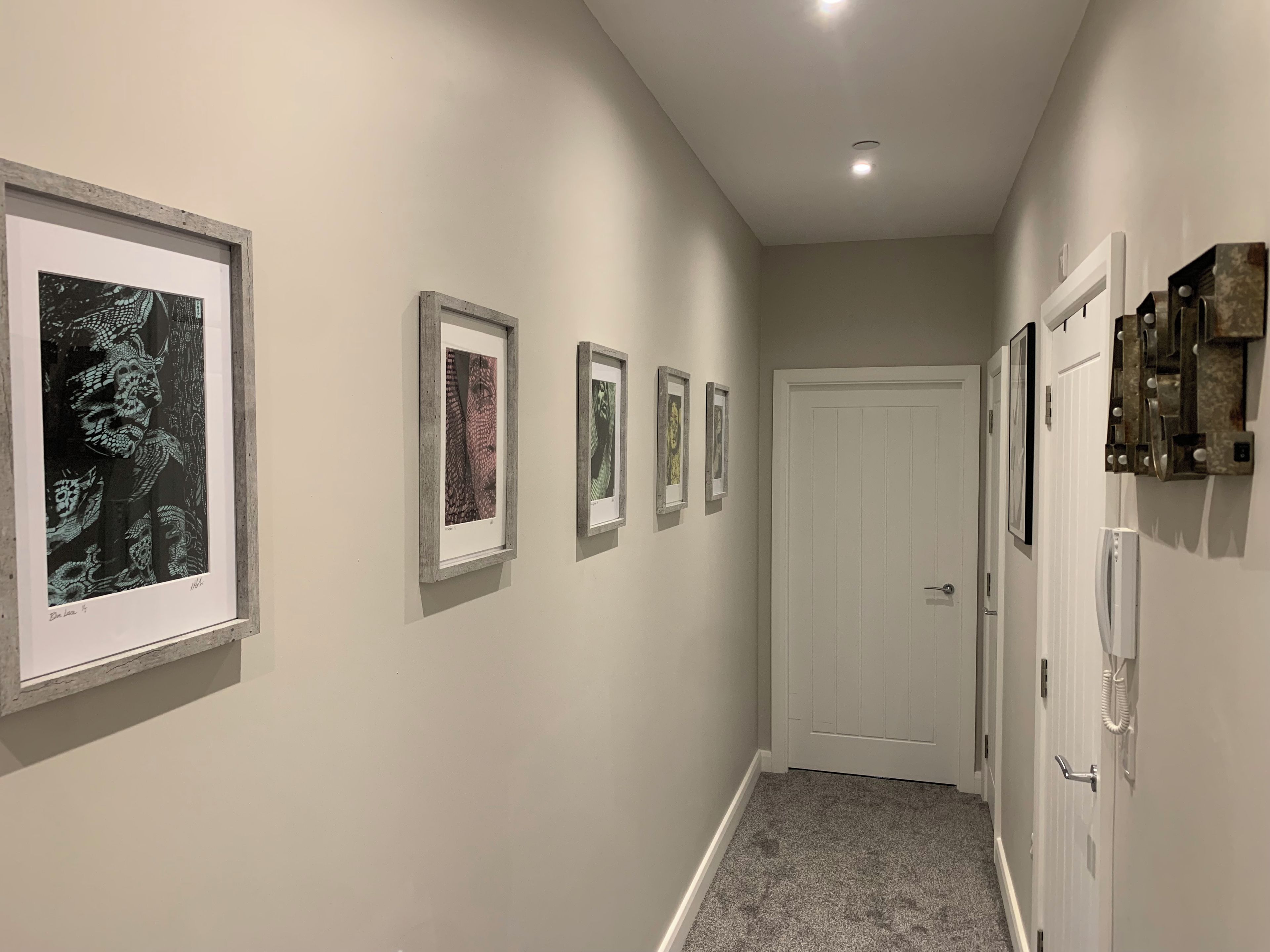 A hallway with framed artwork on the walls, a white door at the end, and a light fixture on the ceiling.