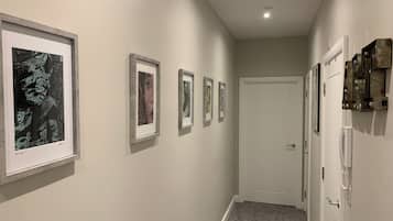 A hallway with framed artwork on the walls, a white door at the end, and a light fixture on the ceiling.