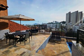 Eine Dachterrasse mit Tisch und Stühlen, einem Sonnenschirm und Blick auf die Stadtlandschaft.