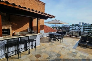 Um terraço no telhado com lareira de tijolos, área de estar ao ar livre e vista da cidade.