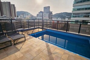 Uma piscina no terraço com vista para edifícios e colinas ao redor.