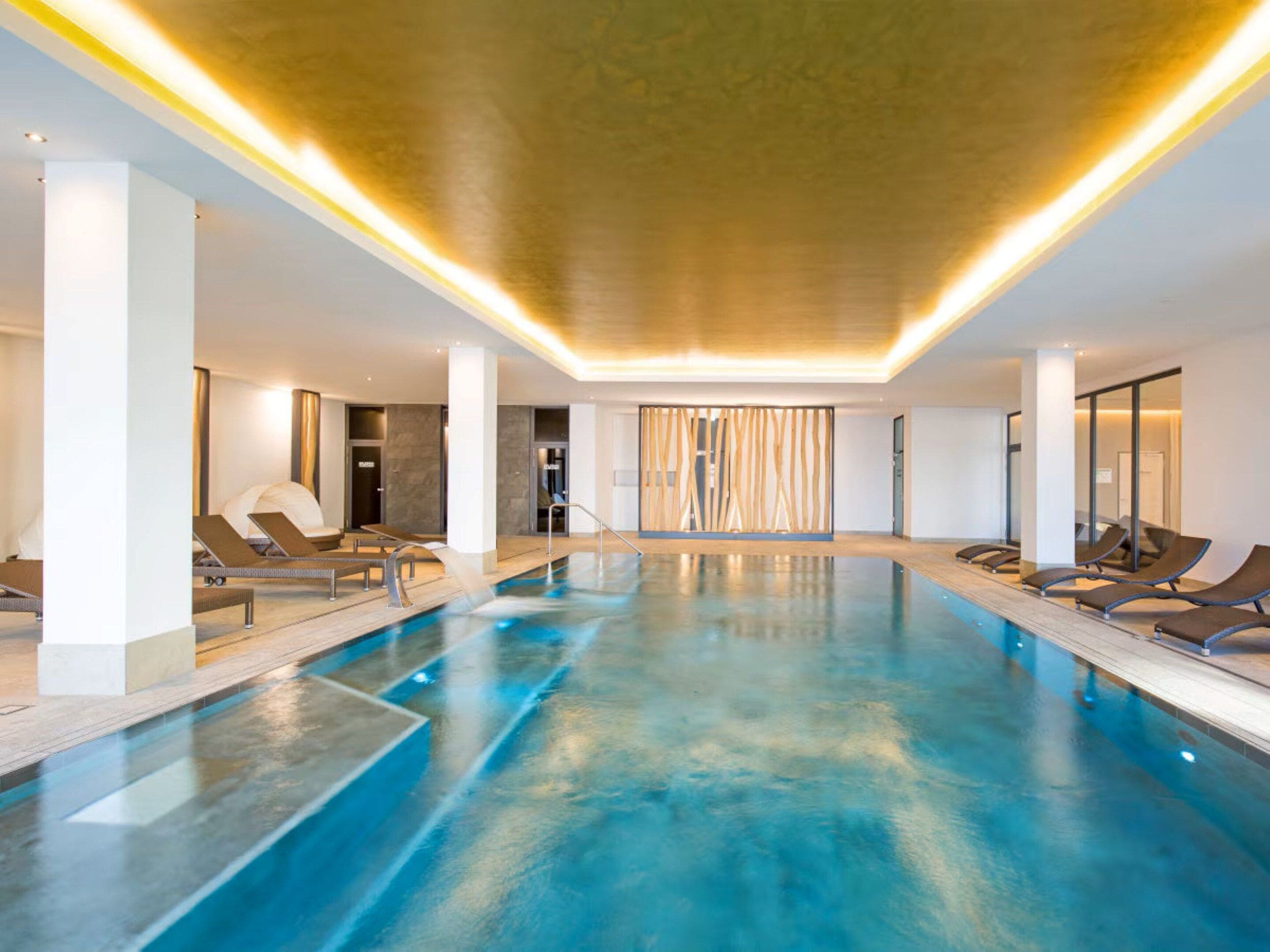 Une piscine intérieure moderne, dotée de chaises longues et d’une eau d’un bleu cristallin.