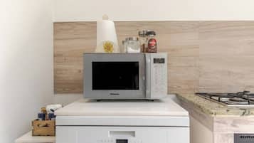 A kitchen with a microwave on top of a white appliance, possibly a coffee maker or a small refrigerator, with a wooden backsplash and a gas stove.