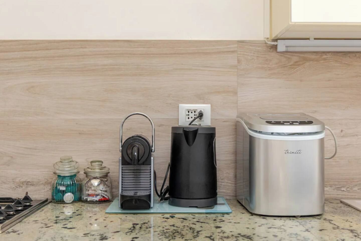 Une cuisine équipée d’une machine à café, d’une bouilloire et d’une bouteille d’eau posée sur le plan de travail.