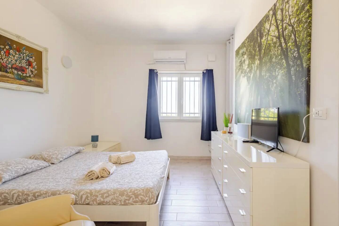 Een slaapkamer met een bed, een dressoir, een televisie en een schilderij.