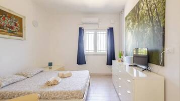 Een slaapkamer met een bed, een dressoir, een televisie en een schilderij.