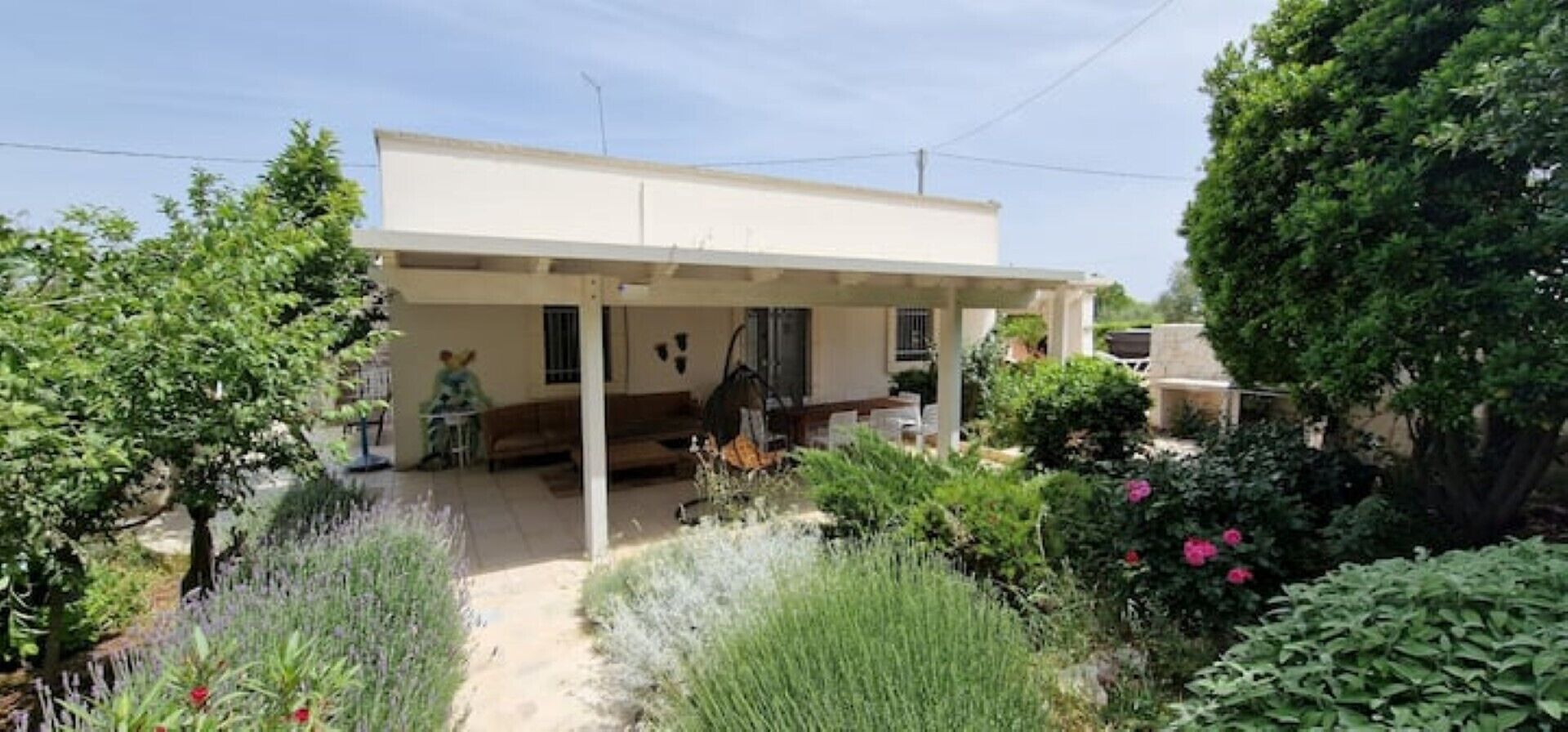 Une maison de plain-pied dotée d’un porche abrité, entourée d’un jardin où poussent diverses plantes et fleurs.