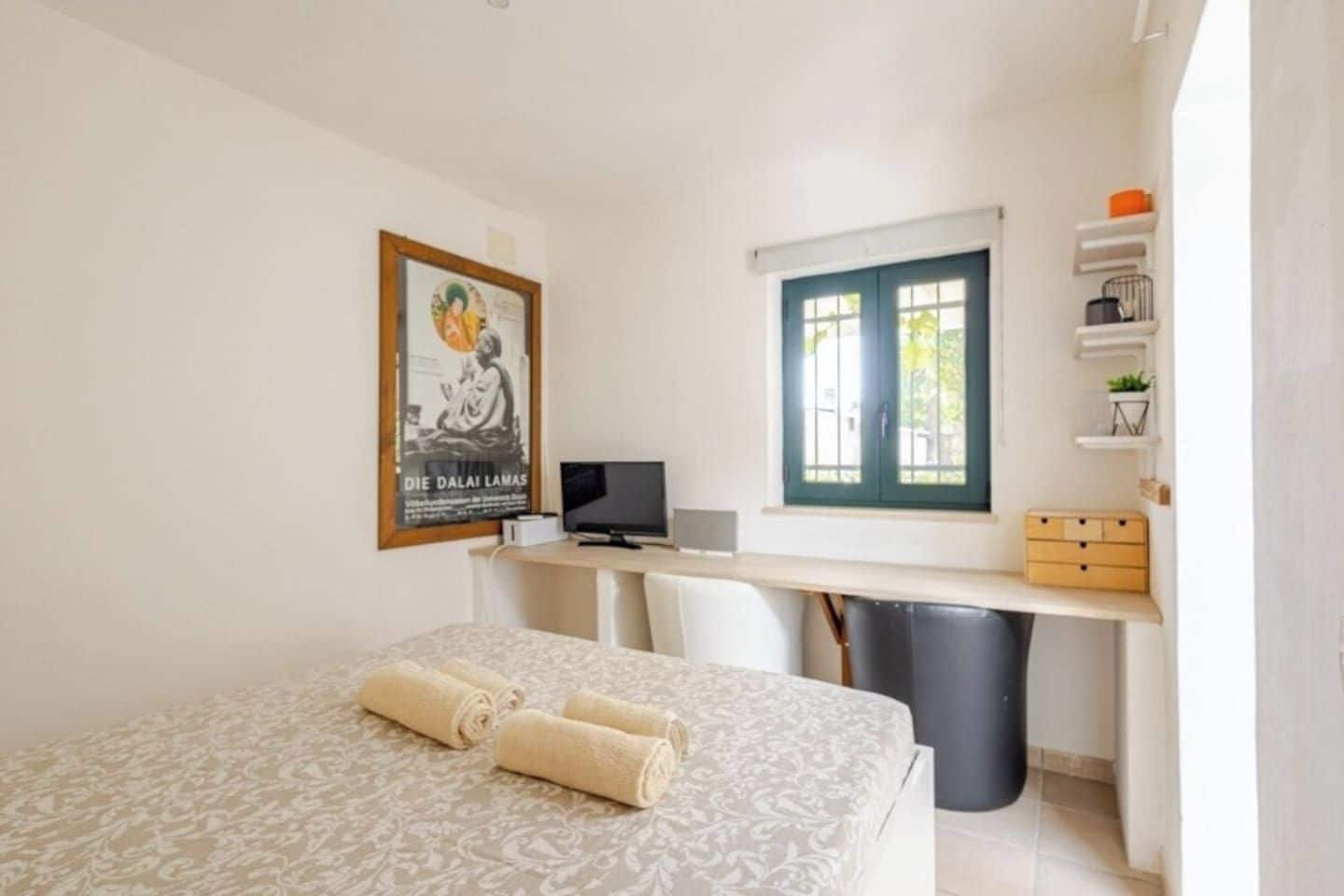 Une chambre d’hôtel avec un lit, un bureau, une télévision, une fenêtre et une affiche au mur.
