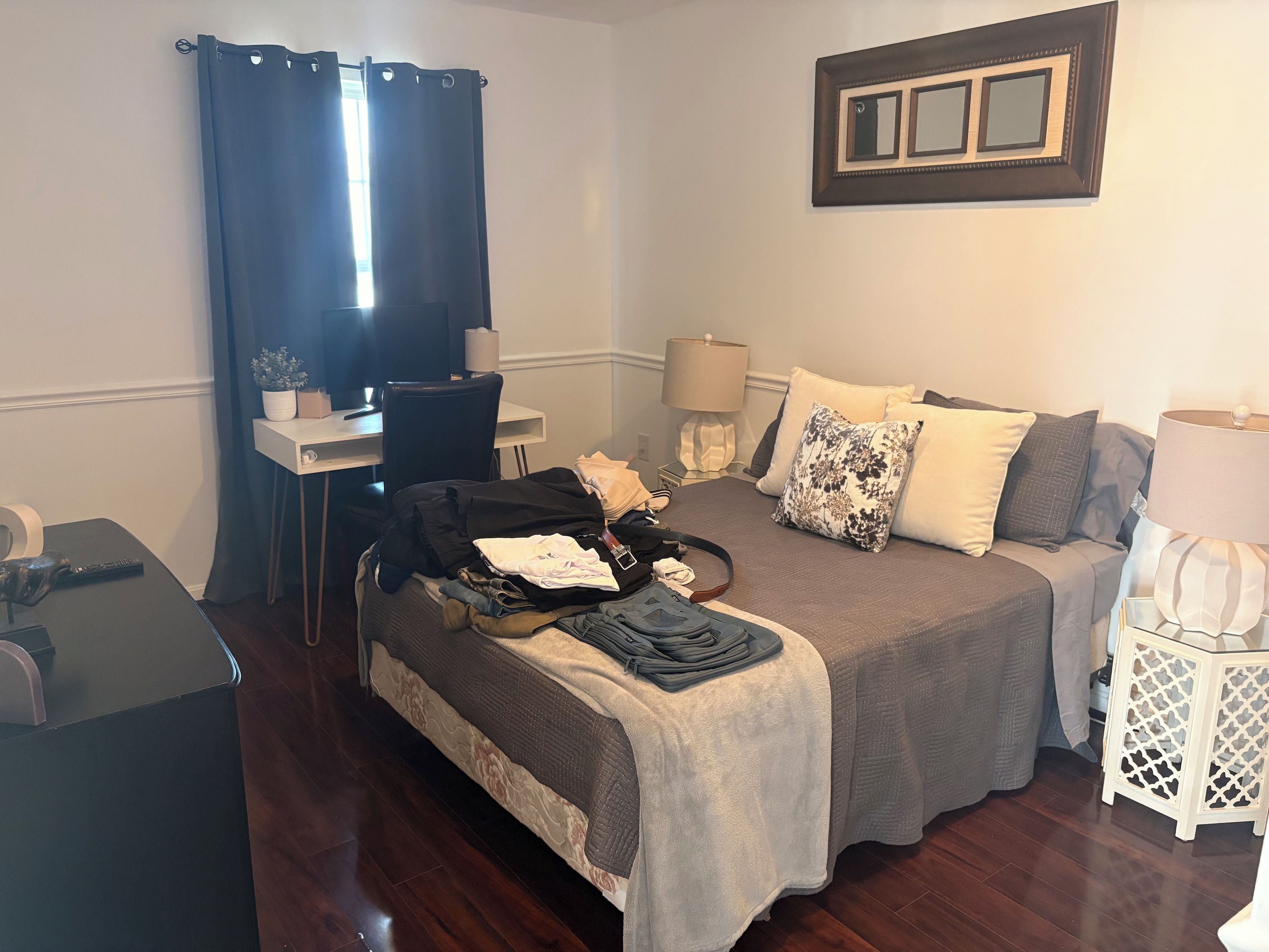 A hotel room with a bed, bedside tables, a desk, a television, and a window with curtains.
